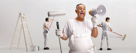 Painter holding a roller and a megaphone and workers painting a wall isolated on white backgroundの写真素材