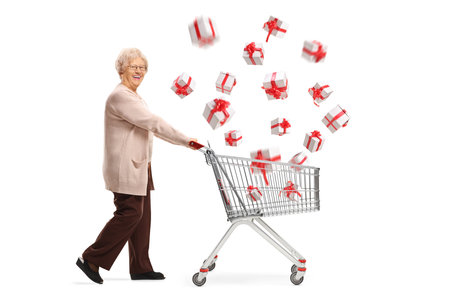 Full length shot of a senior woman pushing a shopping cart with presents flying in the air isolated on white backgroundの写真素材