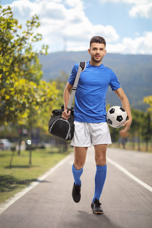 Full length portrait of a football player with a bag walking in a parkの写真素材