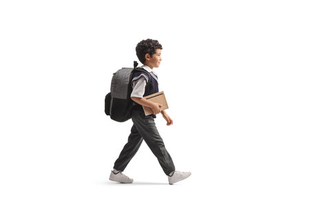 Full length profile shot of an asian schoolboy with a backpack and book walking isolated on white backgroundの写真素材