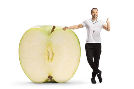 Sports coach with an apple cut in half gesturing thumbs up isolated on white backgroundの写真素材