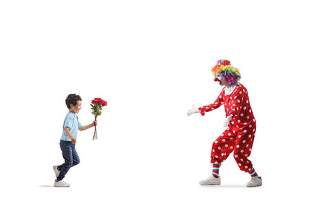 Full length profile shot of a boy bringing flowers to a clown isolated on white backgroundの写真素材