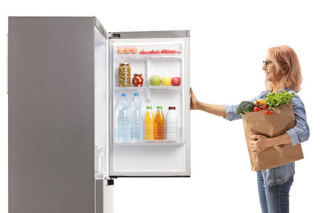 Woman with a grocery bag looking at a fridge isolated on white backgroundの写真素材