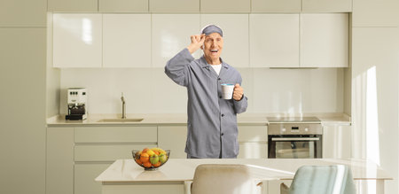Elderly man in pajamas with a sleeping mask holding a cup in a kitchenの写真素材