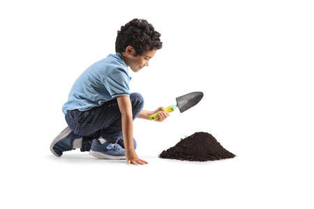 Kid kneeling and digging earth with a spade isolated on white backgroundの写真素材