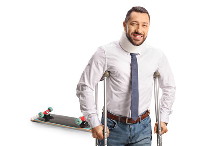 Injured man with crutches, skateboard accident concept isolated on white backgroundの写真素材