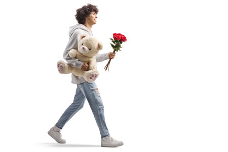Full length profile shot of a guy carrying a teddy bear and red roses isolated on white backgroundの写真素材