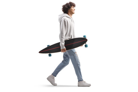 Full length profile shot of a guy walking and carrying a longboard isolated on white backgroundの写真素材