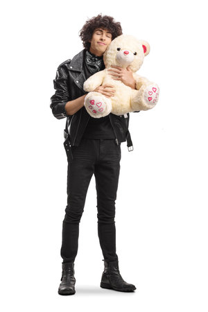 Young man in a leather jacket standing and hugging a teddy bear isolated on white backgroundの写真素材