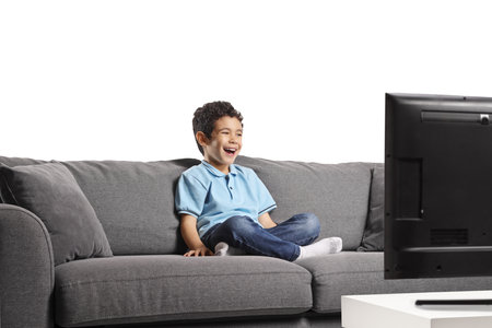Kid sitting on a sofa watching tv and laughing isolated on white backgroundの写真素材