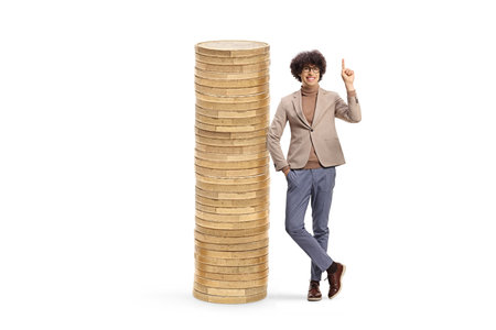 Young man pointing up and leaning on a pile of coins isolated on white backgroundの写真素材