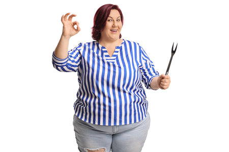 Woman holding a big bbq fork and gesturing ok sign isolated on white backgroundの写真素材