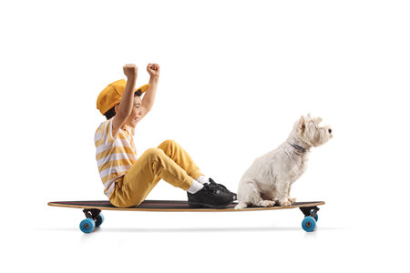Happy boy with a dog sitting and riding on a longboard isolated on white backgroundの写真素材