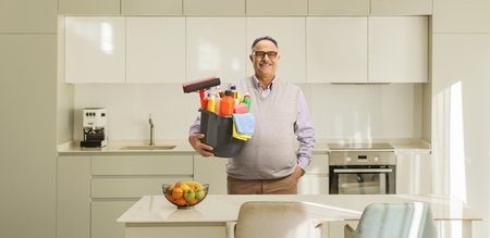 Mature casual man holding a bucket with cleaning supplies in a kitchenの写真素材