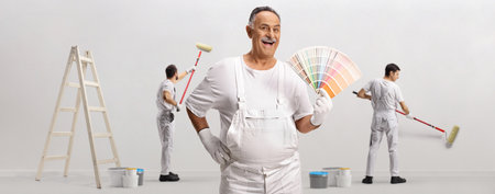 Painter with a color palette and workers painting a wallの写真素材