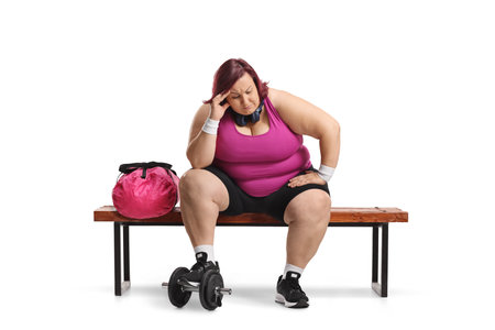 Tired woman in sportswear sitting on a gym bench isolated on white backgroundの写真素材