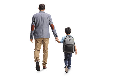 Rear view shot of a father and boy with school backpack holding hands and walking isolated on white backgroundの写真素材