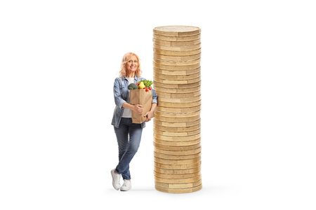 Woman with a grocery bag standing against a pile of coins isolated on white backgroundの写真素材