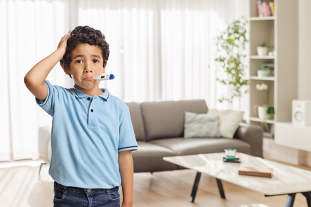 Sick boy with thermometer standing in a living roomの写真素材