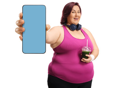 Plus size woman in sportswear holding a green smoothie and a smartphone isolated on white backgroundの写真素材