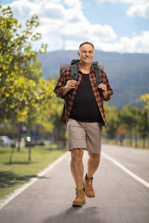 Full length portrait of a cheerful mature hiker carrying a backpack and walking in a parkの写真素材