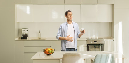 Young man in kitchen holding a glass of waterの写真素材