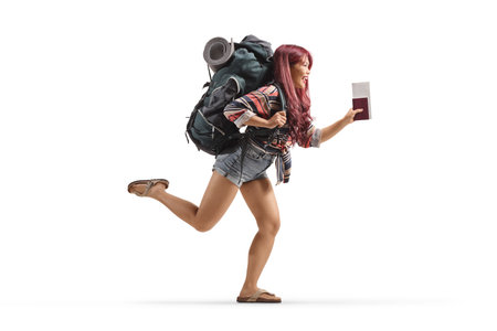 Full length profile shot of a young female traveler with a backpack running and holding a passport isolated on white backgroundの写真素材