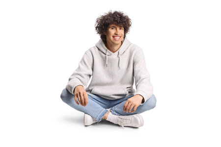 Young man with curly hair sitting with crossed legs isolated on white backgroundの写真素材