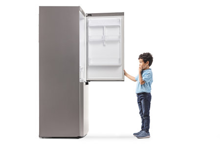 Full length profile shot of a boy looking at an empty fridge isolated on white backgroundの写真素材