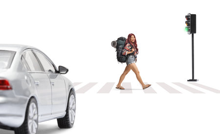 Asian female tourist crossing at pedestrian zebra with a backpack and smiling at camera isolated on white backgroundの写真素材