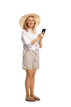 Mature woman with a straw hat holding a smartphone isolated on white backgroundの写真素材