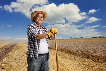 Mature farmer with a straw hat posing on a fieldの写真素材