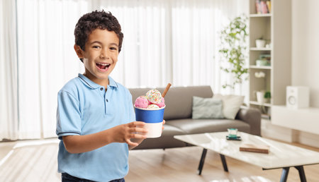 Boy holding an ice cream in a cup at homeの写真素材