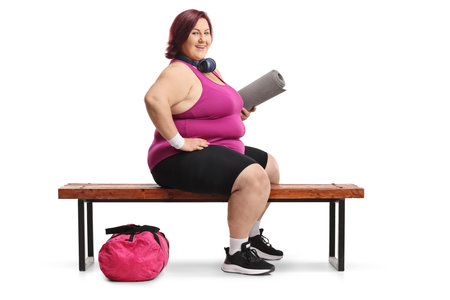 Overweight woman in sportswear sitting on a gym bench isolated on white backgroundの写真素材
