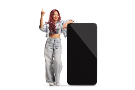 Asian woman leaning on a big mobile phone and pointing up isolated on white backgroundの写真素材