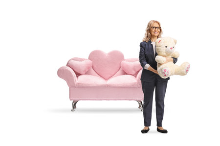 Middle aged woman holding a teddy bear in front of a sofa isolated on white backgroundの写真素材