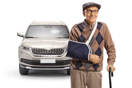 Damaged car and an elderly man with a broken arm wearing a splint isolated on white backgroundの写真素材