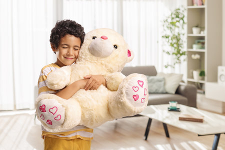 Happy boy hugging a big teddy bear at homeの写真素材