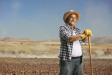 Mature farmer with a straw hat standing on a soil fieldの写真素材