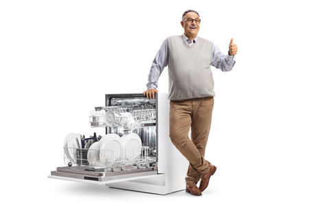 Smiling mature man leaning on a dishwasher and gesturing thumbs up isolated on white backgroundの写真素材