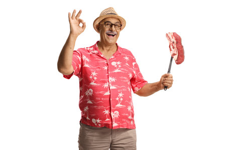 Happy mature man holding raw steak with a fork isolated on white backgroundの写真素材