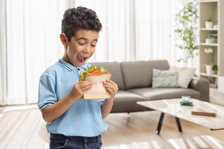 Overjoyed boy eating a tasty sandwich at homeの写真素材