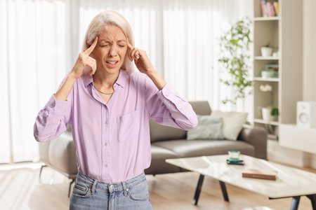 Young woman in a living room suffering from headacheの写真素材