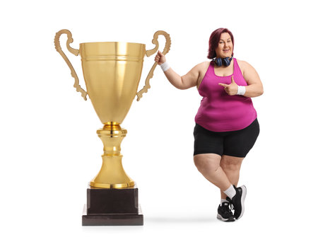 Corpulent woman in sportswear pointing at a gold trophy cup isolated on white backgroundの写真素材