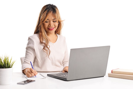 Asian woman writing in a notebook and using a laptop computer isolated on white backgroundの写真素材