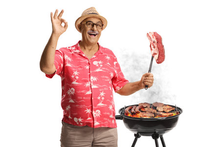 Happy mature man with a bbq and a raw steak on a fork isolated on white backgroundの写真素材