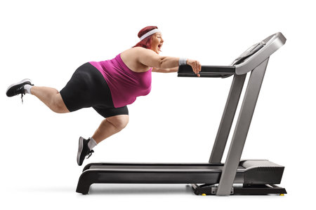 Corpulent woman screaming and holding a treadmill with legs in the air isolated on white backgroundの写真素材