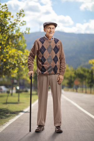 Full length portrait of a senior man standing with a walking cane in a parkの写真素材