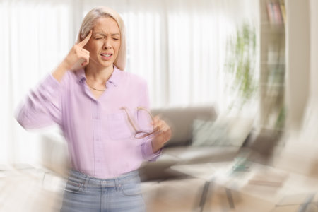 Woman with blurred vision holding glasses at home and feeling dizzy