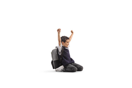Schoolboy sitting on knees and gesturing happiness isolated on white backgroundの写真素材